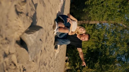 vertical video Silhouette of couple in love sitting on the sandy bank of the river admiring the sun