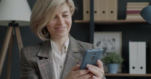 Cheerful Business Lady Using Smartphone Texting Looking at Screen with Happy Smile in Office