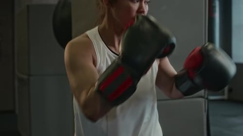 Young Professional Female Boxer Practising on Punch Bag at Gym