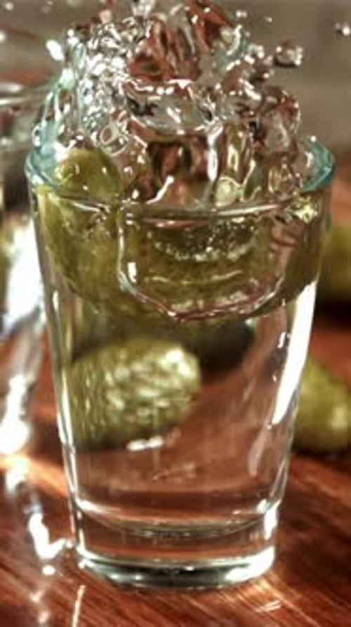 Um pepino em conserva cai em um copo de vodka filmado em uma câmera de alta velocidade a 1000 Fps