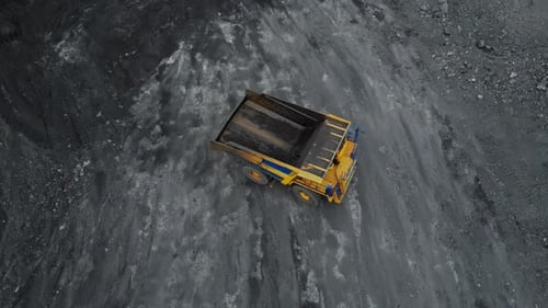 Aerial View of a Loaded Yellow Dump Truck Moving on a Textured Black Coal Mine Surface