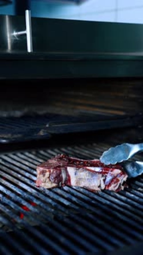 Piece of beef is put on the grill with the help of tongs. Cooking meat on the charcoals.