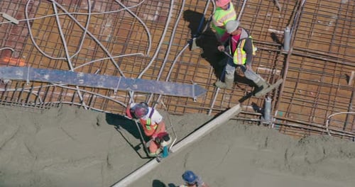 Blick von oben auf eine Baustelle, während Bauarbeiter Zement auf das Dach gießen.