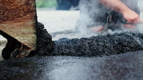 Road construction workers manually Spread and adjust hot tar or asphalt on the ground at the