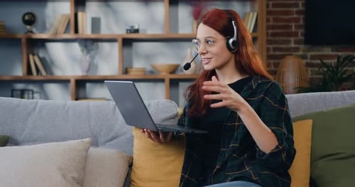 Young woman in headphones, talking video call, sitting on the sofa at home. Online education