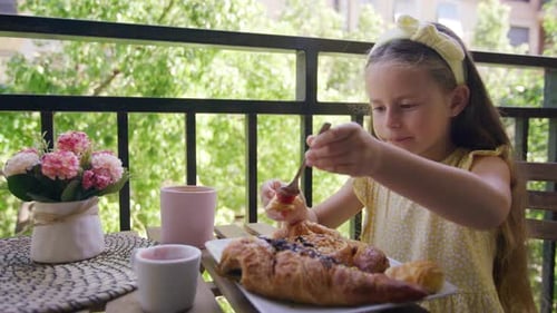Girl Eats Croissant with Jam on Balcony