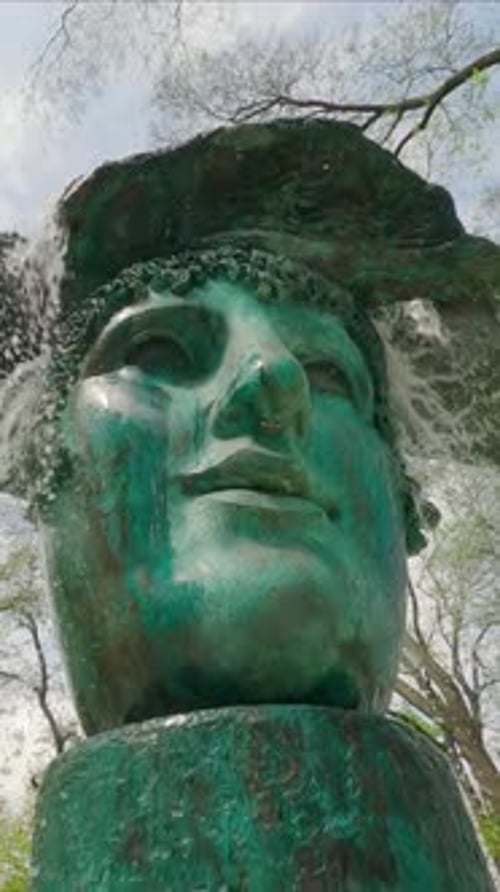 bronze fountain in city park against background of trees and cloudy sky