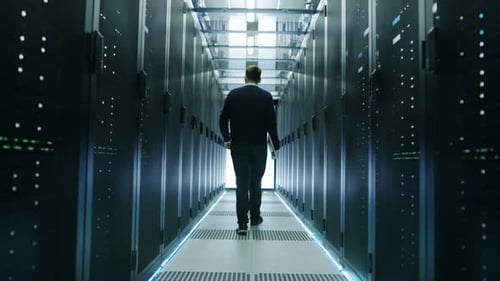 Vista posterior de un ingeniero de TI recorriendo un centro de datos con servidores en rack en funcionamiento.