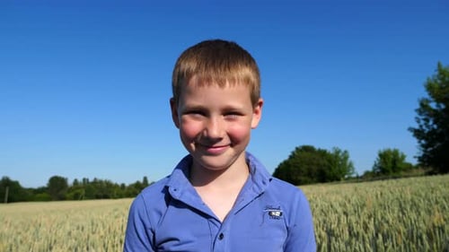 Little Smiling Boy with Freckles Looks Into Camera Against Background of Wheat Field Portrait of