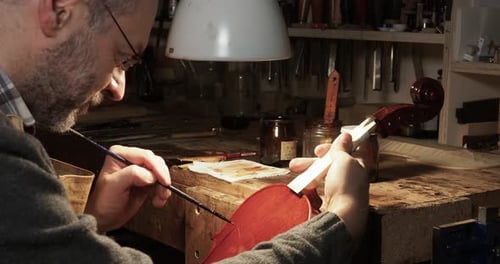 Close up of a violin maker carefully applying varnish on a new handcrafted violin in Cremona, Italy
