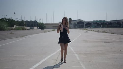 Young Girl Caucasian Woman in Short Black Dress Walking Facing Forward in an Industrial Area on the