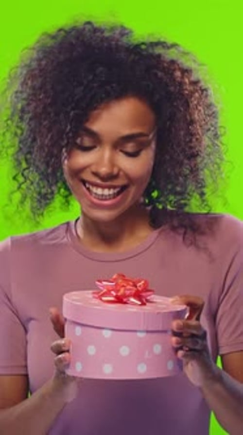 Young Woman Opening Pink Gift Box on Green Background