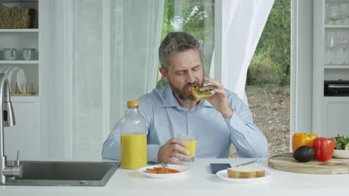 Man Eating Sandwich and Drinking Orange Juice Indoors