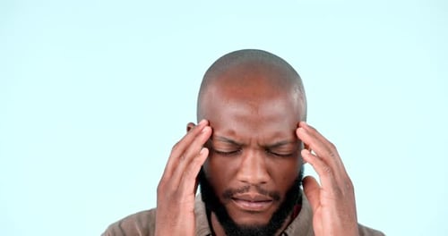 Man, headache and frustrated with pain in studio for stress, vertigo and burnout on blue background