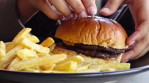 Hand Holding Beef Burger on Table Close Up