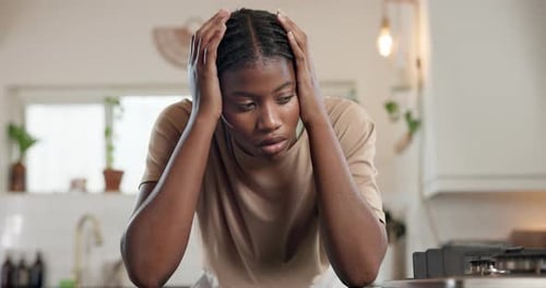 Worried Woman in Kitchen Holding Head in Hands