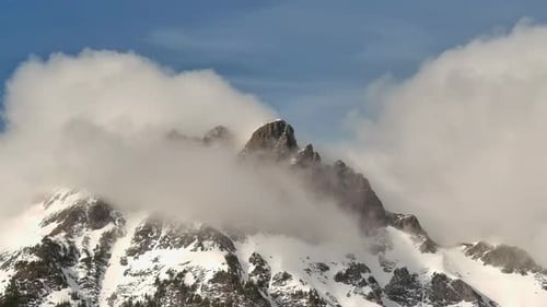 Rugged Snowy Mountain Peak surrounded by fog and Clouds. Sun and blue sky. Spring Season. British Co