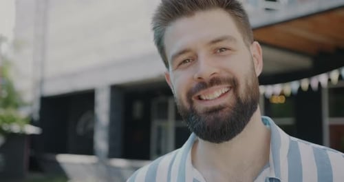 Joyful Bearded Guy Smiling and Looking at Camera Outdoors in City Street in Summer