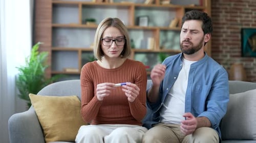Trauriges Ehepaar führt auf dem Sofa einen Schwangerschaftstest mit negativem Ergebnis durch