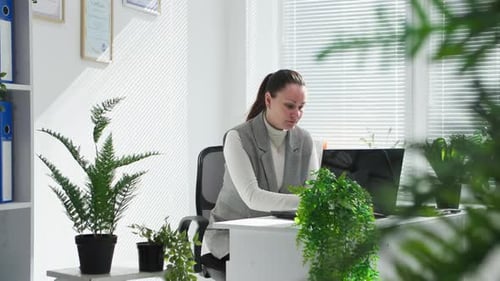 Jeune femme travaillant avec des documents sur ordinateur au bureau avec des plantes vertes