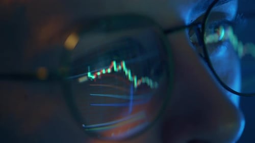 Trader Wearing Glasses is Working on Laptop Computer Screen with Stock Market Charts and Bitcoin BTC