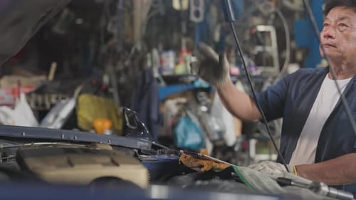 Side view senior Asian technician or garage worker stand and work in front part of car machine