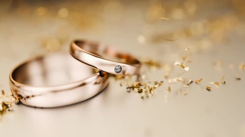Gold rings stand on a metal surface. The camera zooms in on the wedding rings.