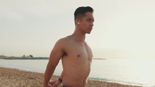 Young athletic man standing on the beach doing muscle stretching before training