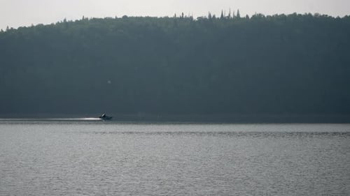 View From Coast of Speedboat Sailing Across Lake on Background of Rolling Hills of Green Trees on
