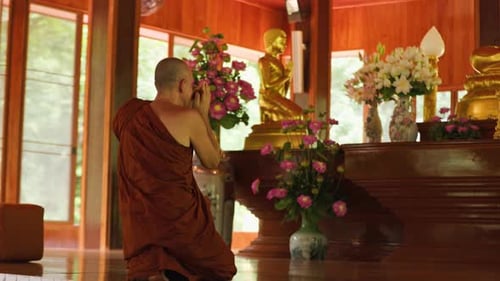 Un moine bouddhiste rend hommage devant une statue de Bouddha à l'intérieur d'un temple