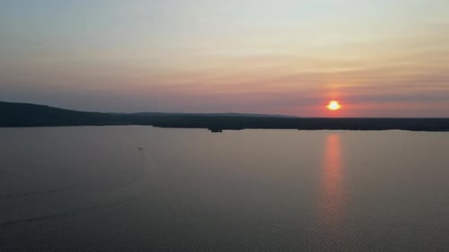 Flying over lake with boat driving towards beautiful suset