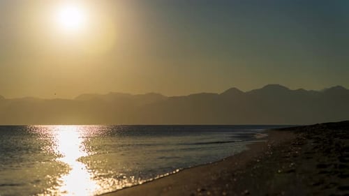 Timelapse, Sunset on the sea. The sun is setting behind the mountains. On A Sandy Empty Beach.