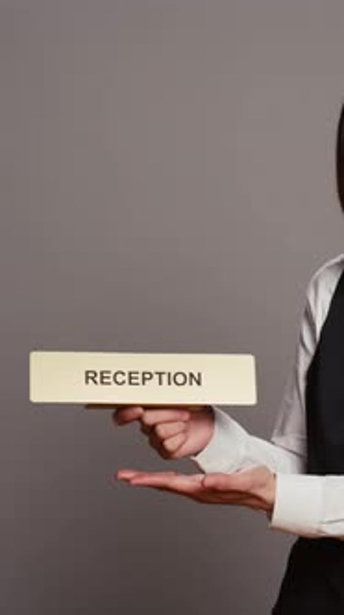Vertical Video Hotel Concierge Holding Sign to Indicate Direction for Reception Desk