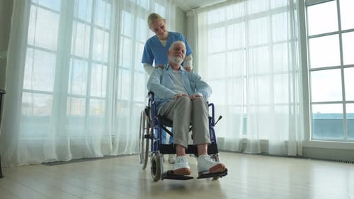 Caregiver Attends Senior Man in Wheelchair Indoors