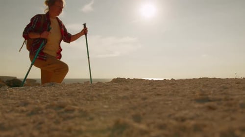 Women tourists climb to top of rocky shore passing against background of sky