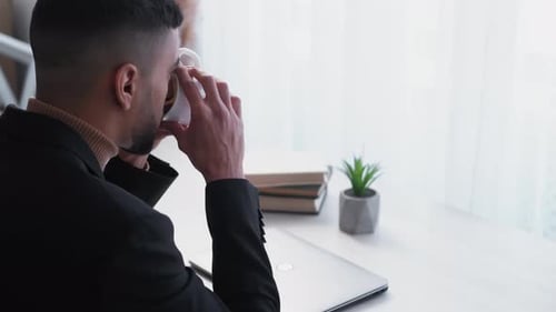 Young Adult Drinking From Cup at Desk