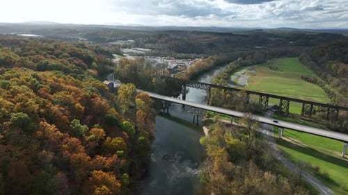 Drone flight over river with bridge in colorful landscape in autumn. Forest with colored leaves in s
