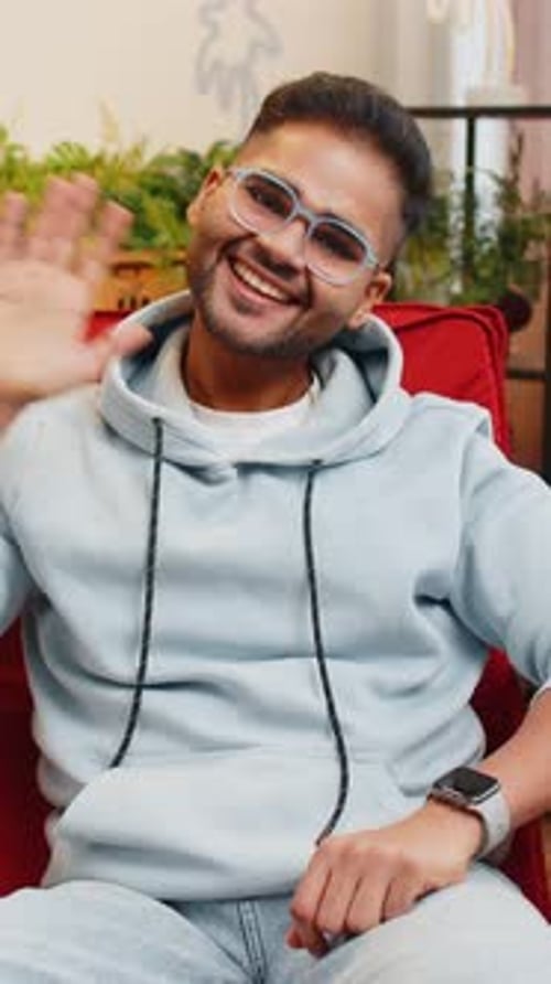 Smiling Man Waving Hello Indoors on Red Chair