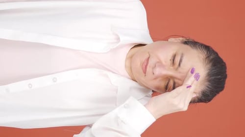Woman Holding Head in Pain on Orange Background