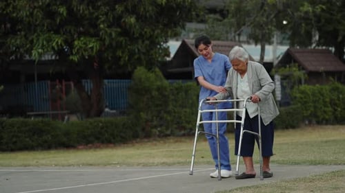 caregiver nurse support senior woman walking with walker in the park