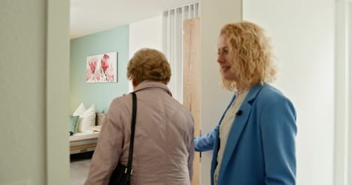 Woman Escorting Senior Into Apartment with Suitcase