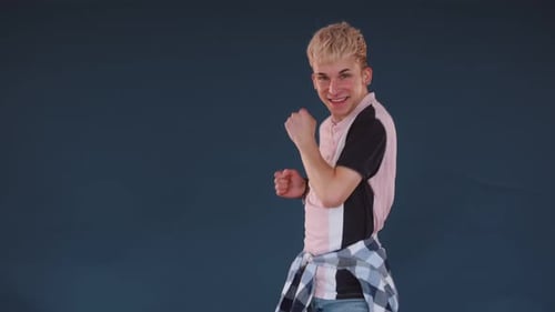 Caucasian handsome young man in pink t-shirt, dancing freely, moving to music, having fun, smiling,