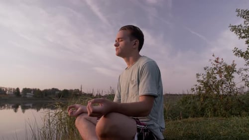 Young Adult Meditating by the Lake at Sunset