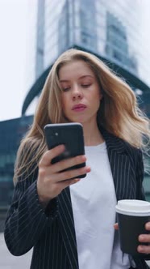 Young Blonde Woman Checking Smartphone While Drinking Coffee on City Walk