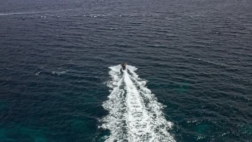 Jet ski rides through the open blue ocean, creating a white trail behind