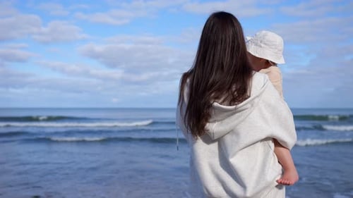 Mama Strolling Along Beach with Charming Little Girl in Arms