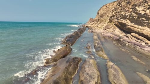 Drone footage of rocky shore with small waves and sunlight in beautiful mediterranean sea 4K