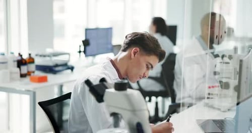Scientist Writing Notes Next to Microscope in Lab
