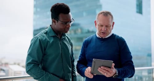 Men Discuss Tablet on Urban Balcony