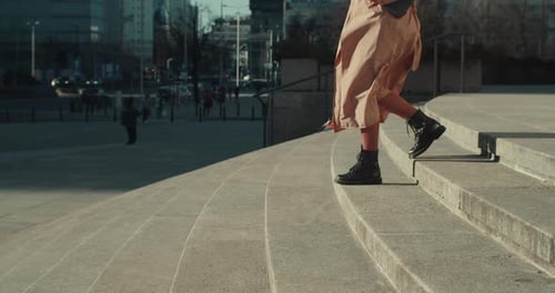 Side View Legs of Beautiful Woman in Beige Autumn Coat Black Shoes Walking Down Sunny City Square